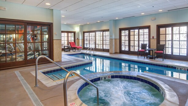 A swimming pool with a hot tub, lounge chairs, and a glass-enclosed area with exercise equipment.