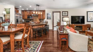 A spacious living area with a wooden dining table, bar stools, a sofa, and a television.