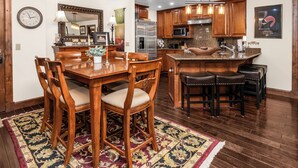 A modern kitchen with wooden cabinets, stainless steel appliances, and a dining area with a wooden table and chairs.