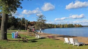 Un parque junto al lago con un parque infantil, sillas de descanso y una terraza de madera.
