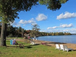 A lakeside park with a playground, lounge chairs, and a wooden deck. - Northern Resort #17 (Minocqua)