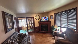 Un salón con sofá, sillón, chimenea, televisor y vistas a través de un ventanal corredera.