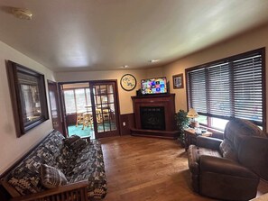 A living room with a sofa, armchair, fireplace, television, and a view through a sliding door. - Northern Resort #17 (Minocqua)