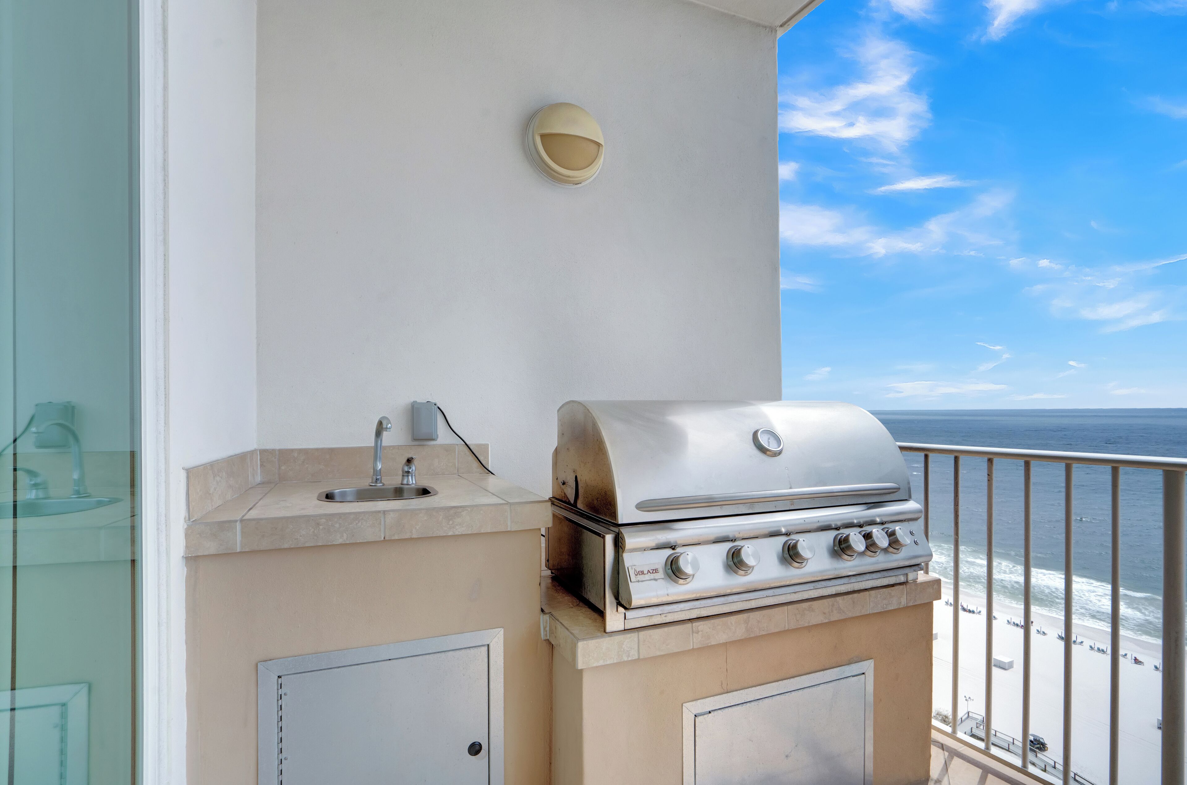 Een balkon met een roestvrijstalen barbecue, een klein spoelbakje en een wandlamp.