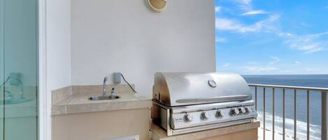 Een balkon met een roestvrijstalen barbecue, een klein spoelbakje en een wandlamp.