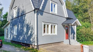 Ein zweistöckiges Haus mit grauer Fassade, einer roten Tür und einer kleinen Veranda.