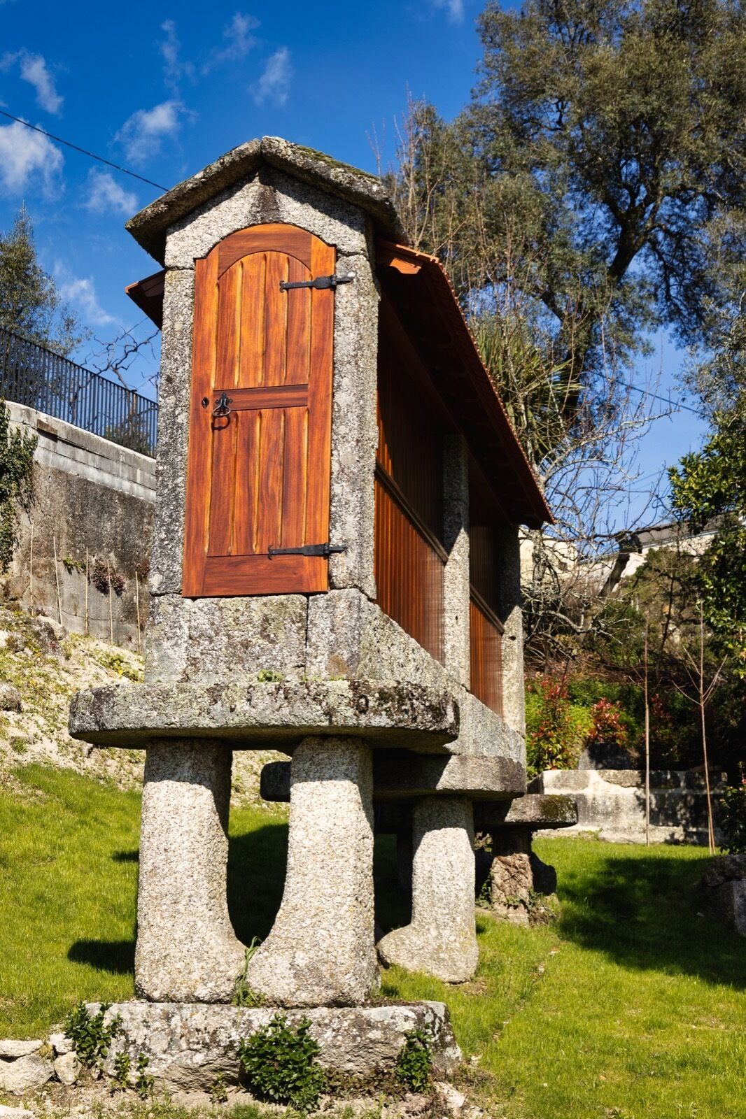A stone structure with a wooden door, possibly a historical building or monument, surrounded by greenery and trees.