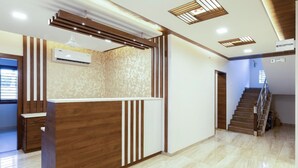 Un espace d’accueil avec un comptoir de réception en bois, un mur décoré de motifs et un escalier menant à l’étage supérieur.