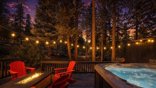 A hot tub surrounded by red chairs on a wooden deck, with string lights and a forest backdrop. - Navigate Stays Hot Tub Home 5 Min to Ski Resort (Big Bear Lake)