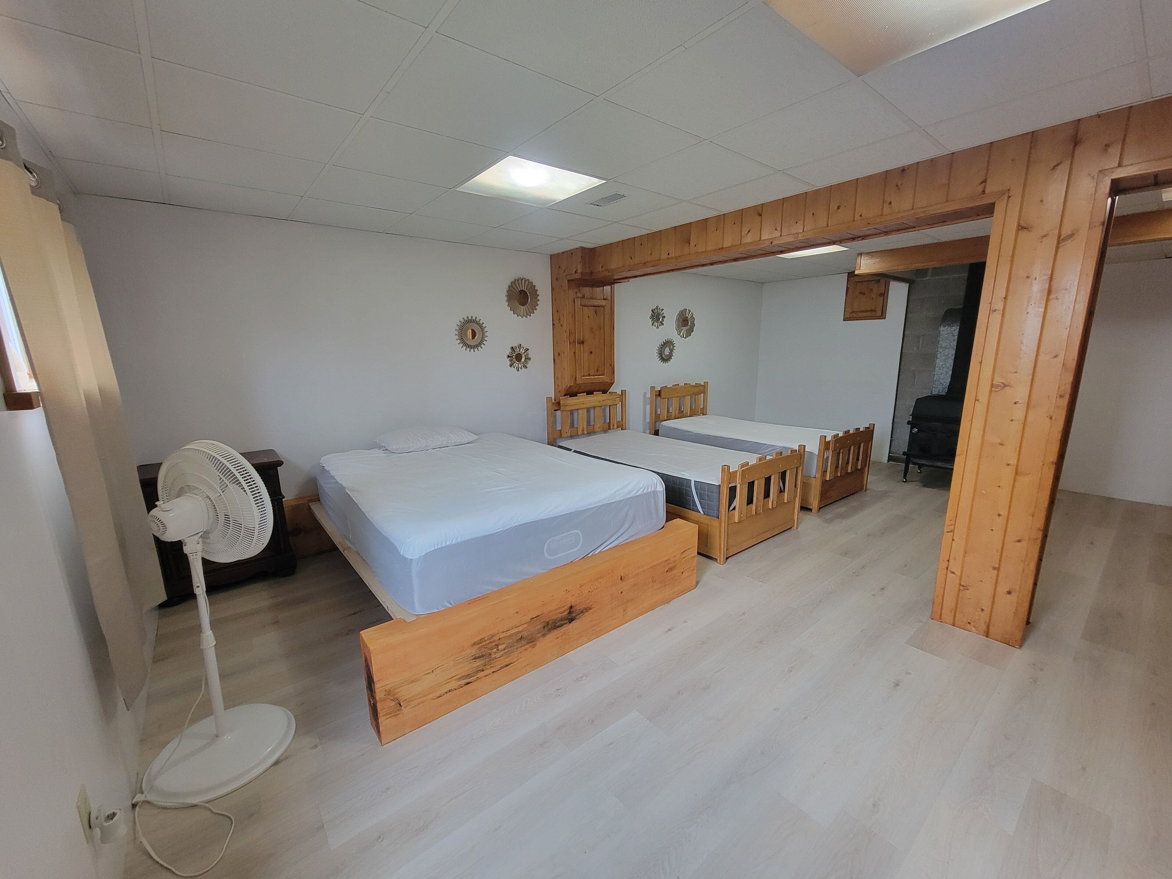A bedroom with two single beds, a wooden floor, a standing fan, and a small table.