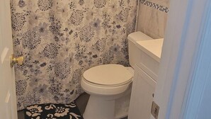 Un baño pequeño con inodoro, cortina de ducha y piso de baldosas.