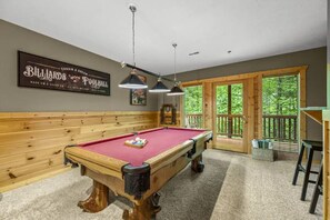A pool table with a red felt surface, overhead lighting, and a billiard cue rack.