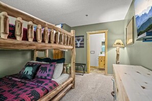 A room with a bunk bed, a desk, a chair, a lamp, and a painting on the wall.