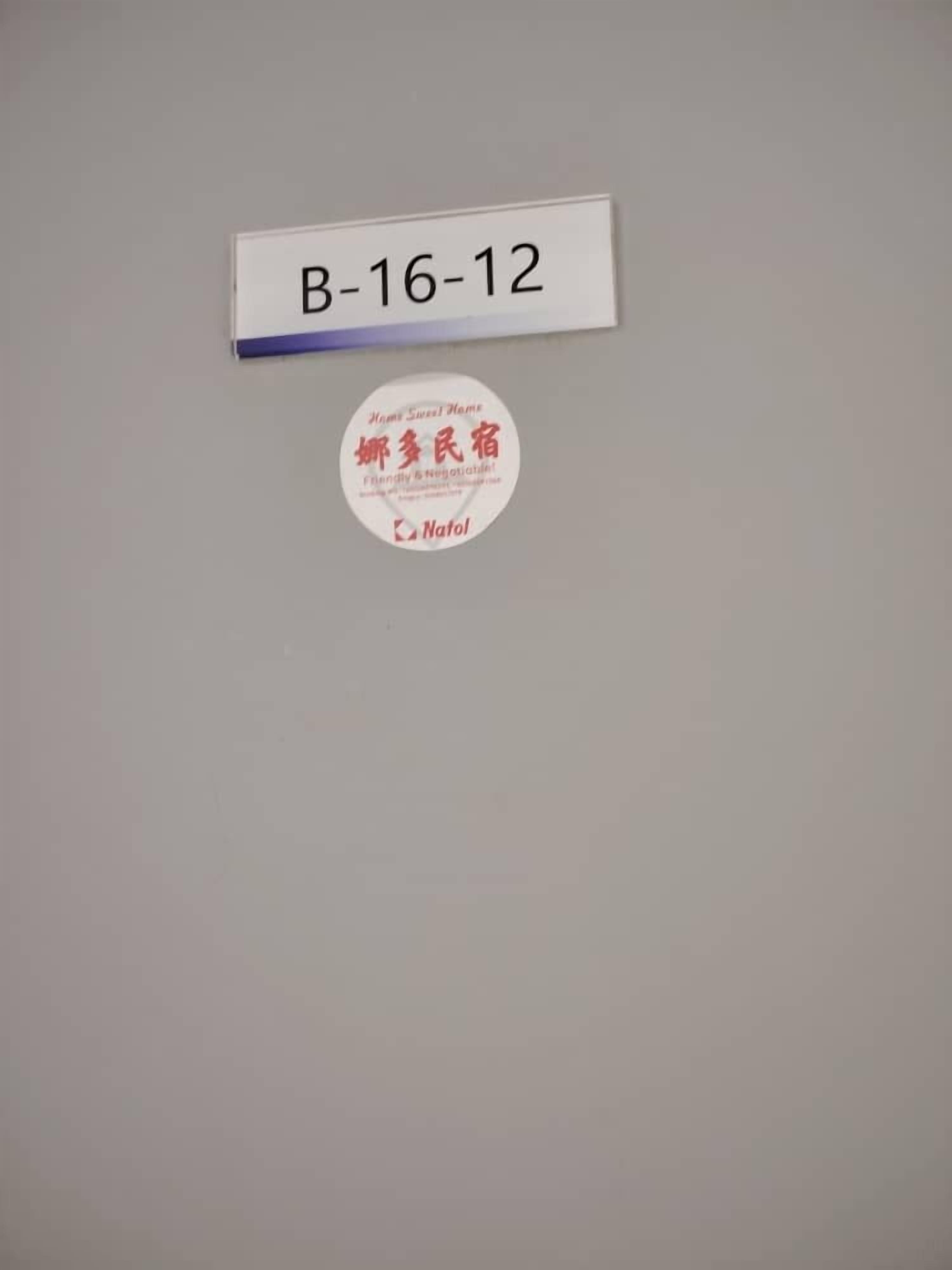 Een kamer met een witte muur, een naambordje met de tekst 'B-16-12' en een rond sticker met Chinese karakters en het woord 'Nafol'.