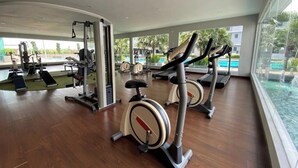 A gym with cardio machines, weight machines, and a pool visible through the windows. - Paradigm Mall Platino 2BR 2FREE By Natol (Johor Bahru)