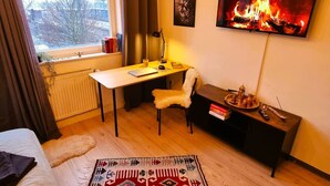 Une petite pièce comprenant un lit, un bureau avec une chaise, un téléviseur fixé au mur et un radiateur.
