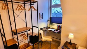 Une petite pièce comprenant un bureau, une chaise et un portant à vêtements.