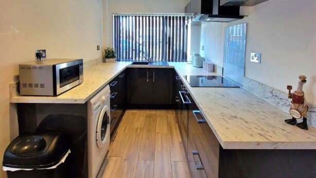 A modern kitchen with a built-in washing machine, a microwave, and a sink. - Charming 3 Bedroom House in Sheffield (Sheffield)
