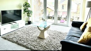 A living room with a flat-screen TV, a glass coffee table, a sofa, and a potted plant. - Charming 3 Bedroom House in Sheffield (Sheffield)