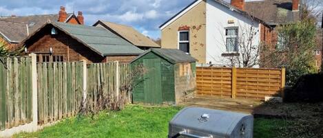A backyard with a barbecue grill, a wooden fence, and houses in the background.