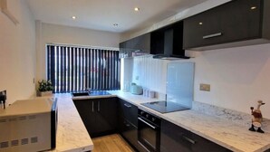 A modern kitchen with dark cabinetry, a marble countertop, and built-in appliances. - Charming 3 Bedroom House in Sheffield (Sheffield)