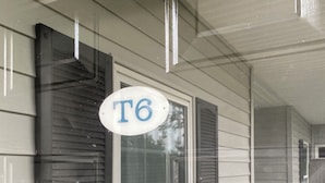 Ein Haus mit einem 'T6'-Schild, einem Fenster mit dekorativem Griff und einer Eingangstür mit einem Fliegengitter.