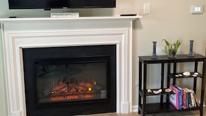 Ein Wohnzimmer mit Kamin, einem darüber hängenden Fernseher und einem kleinen Tisch mit Dekoration.