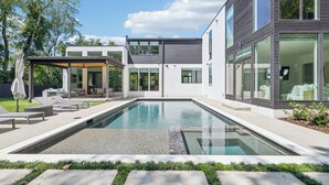 Una casa moderna con piscina, mobiliario exterior y un patio cubierto.