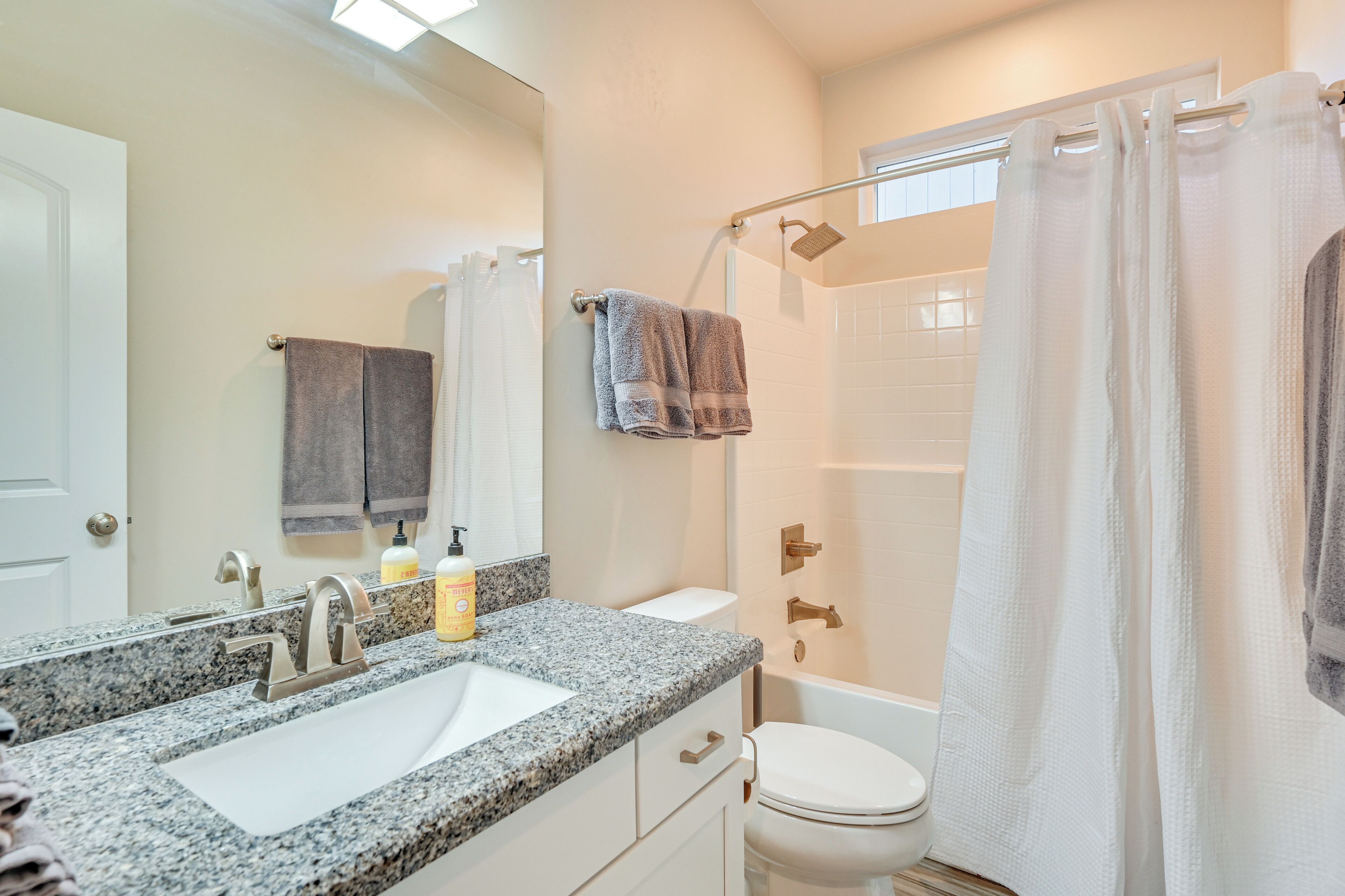 Un baño con lavamanos de encimera de granito, inodoro blanco y zona de ducha con puerta de cristal.