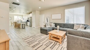 A spacious living room with a grey sectional sofa, a wooden coffee table, and a striped rug. There is a kitchen in the background with white cabinets and a dining area with wooden chairs. - Family-friendly Flagstaff Home Near Hiking Trails! (Flagstaff)