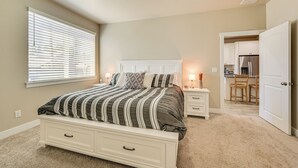 A bedroom with a bed, bedside tables, a nightstand, a window with blinds, and a door leading to a kitchen. - Family-friendly Flagstaff Home Near Hiking Trails! (Flagstaff)