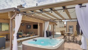 A hot tub under a pergola with string lights, a dining area with chairs, and a covered patio with a table and chairs. - Roomy Tucson Home w/ Hot Tub & Pickleball Court! (Tucson)