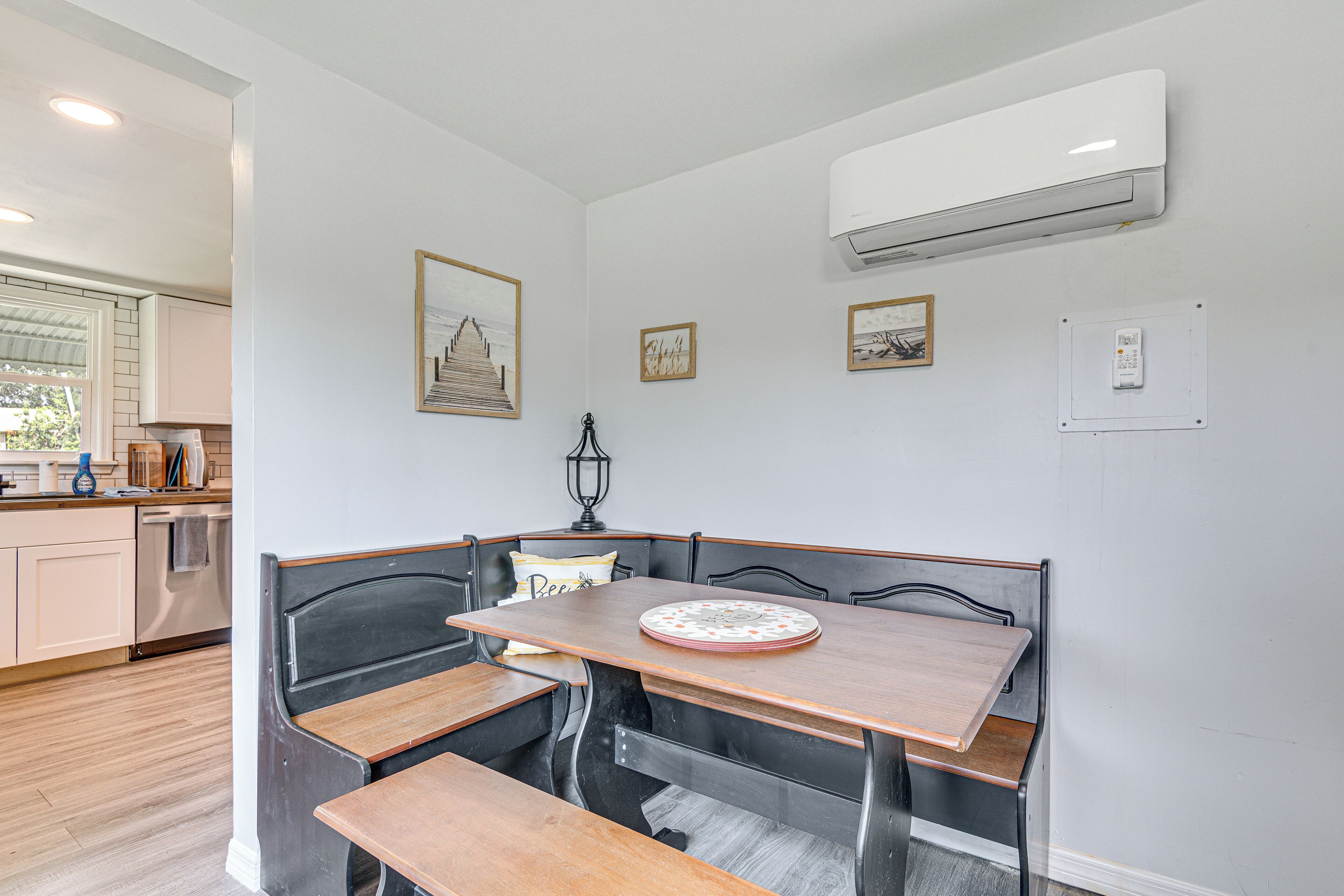 Een eetgedeelte met een houten tafel en banken, een wandairconditioner en lijstjes met foto's aan de muur.