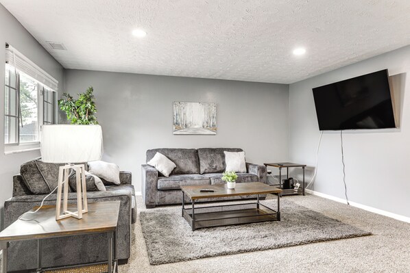 A living room with a gray sofa, a coffee table, a TV, and a plant.