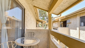 A balcony with a glass table and chairs, a wooden railing, and a view of neighboring buildings. - Oceanside Condo w/ Pool & Hot Tub Access! (Oceanside)
