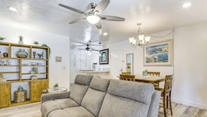 A living room with a grey sofa, wooden shelves, and a dining area with a wooden table and chairs. - Oceanside Condo w/ Pool & Hot Tub Access! (Oceanside)