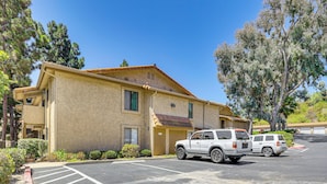 A building with a parking lot, two white SUVs parked, and a clear blue sky. - Oceanside Condo w/ Pool & Hot Tub Access! (Oceanside)