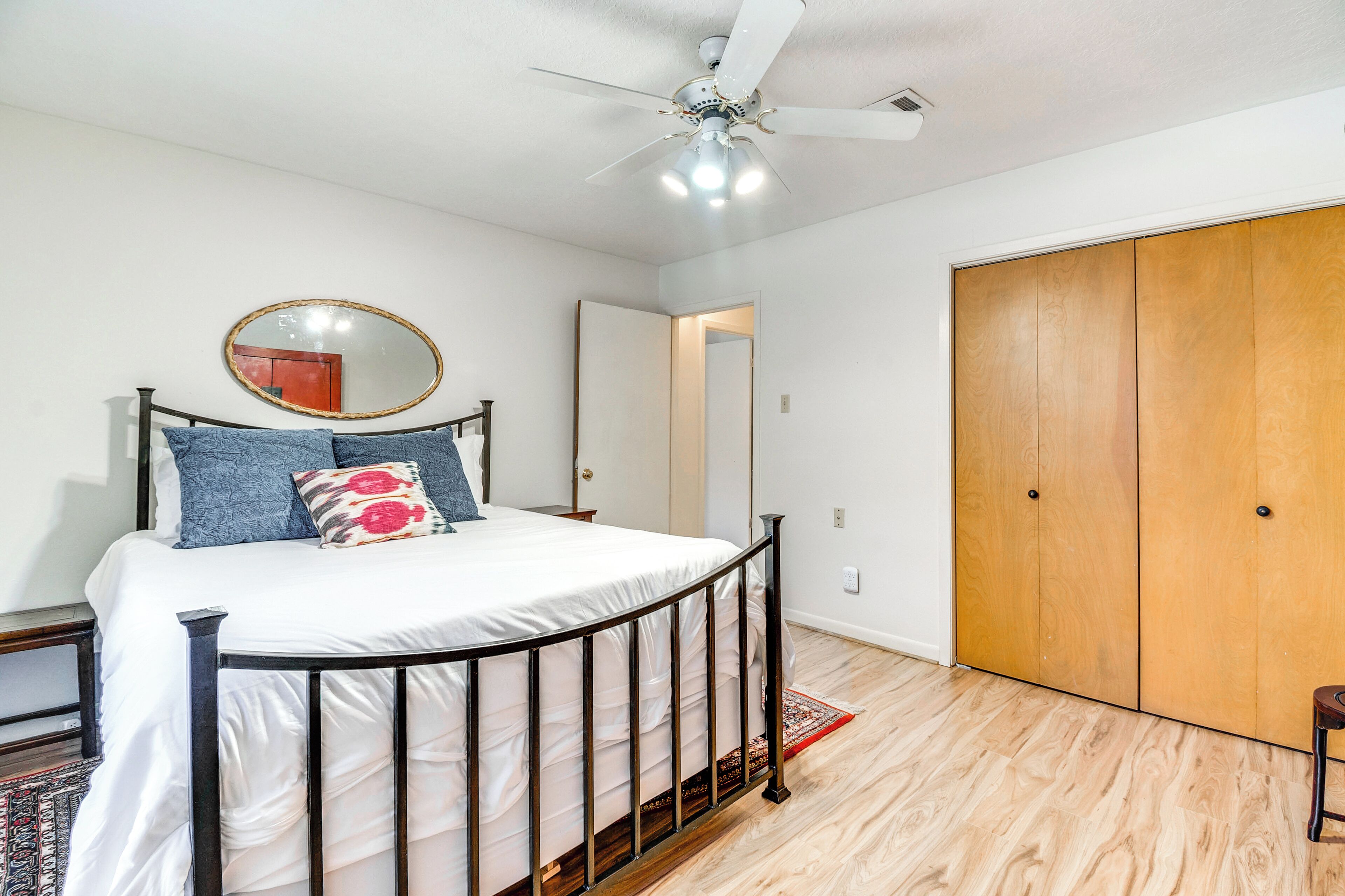 A bedroom with a bed, a ceiling fan, a wooden wardrobe, and a mirror on the wall.