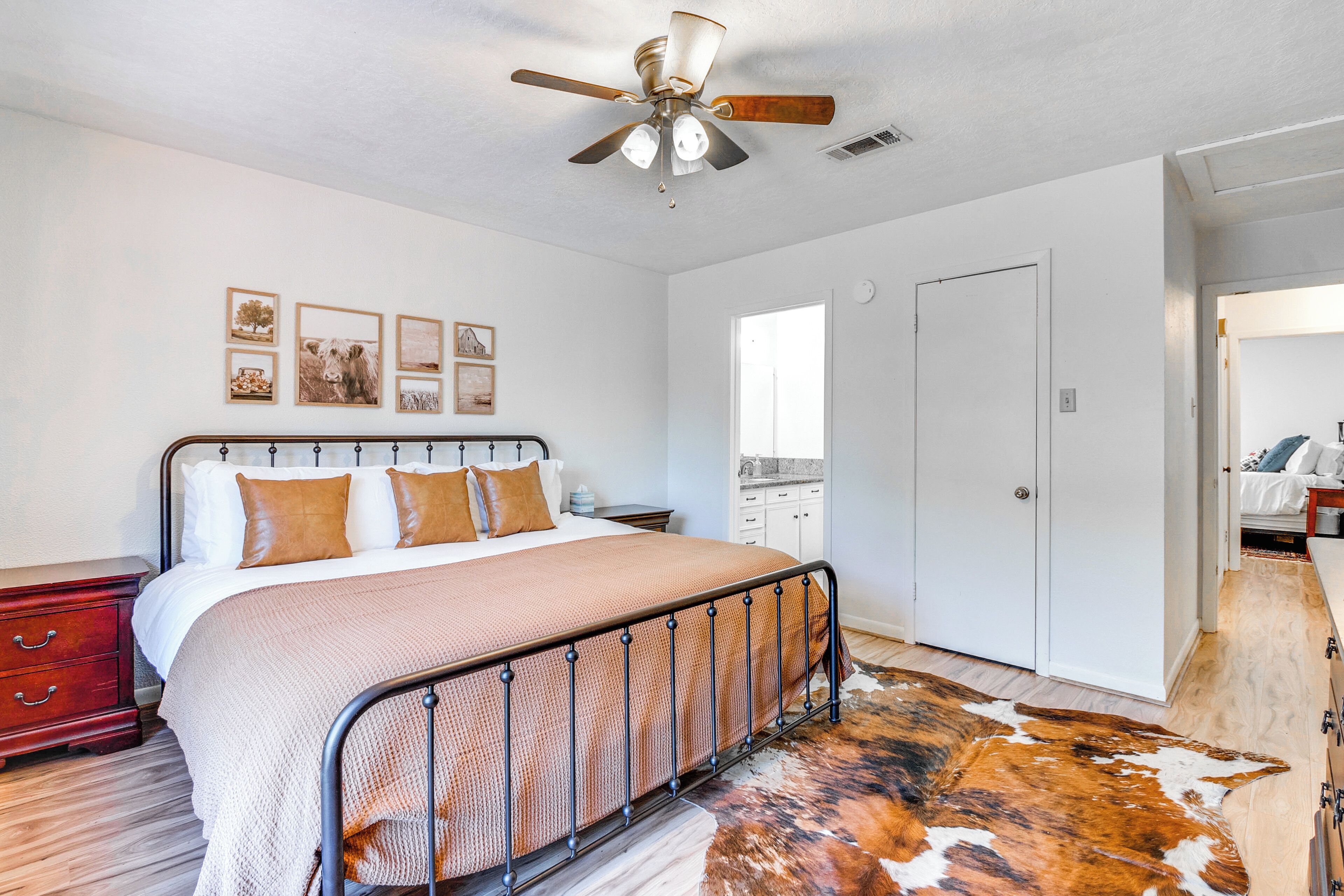 Une chambre à coucher comprenant un lit, un ventilateur de plafond, une table de chevet en bois, une commode, une porte et un tapis en peau de vache.