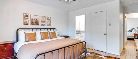 Une chambre à coucher comprenant un lit, un ventilateur de plafond, une table de chevet en bois, une commode, une porte et un tapis en peau de vache.