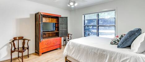 Une chambre à coucher avec un lit, un ventilateur de plafond, une fenêtre et une commode en bois.