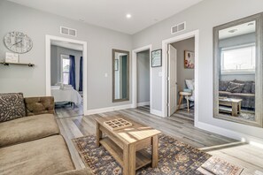 Un salon spacieux avec une table basse en bois, un canapé et un tapis à motifs. Des portes donnent accès aux autres pièces, et un grand miroir reflète l’ensemble de la pièce.