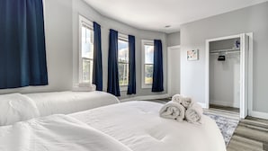 Ein Hotelzimmer mit zwei Betten, einem begehbaren Kleiderschrank und großen Fenstern mit Vorhängen.