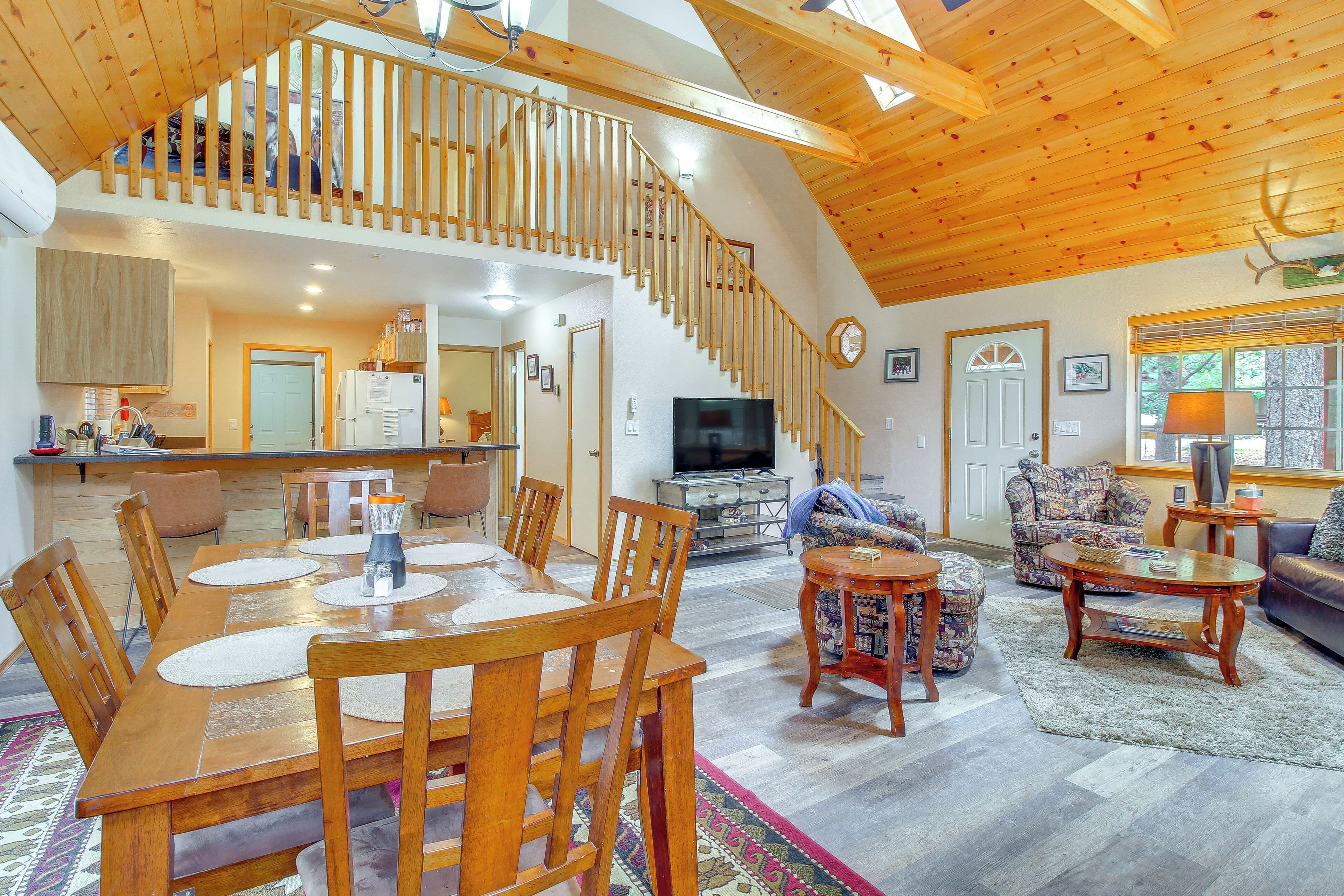 A spacious living area with a wooden staircase, a dining table with chairs, a sofa, and a television.