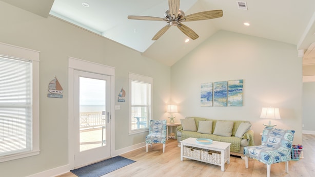 A spacious living room with a high ceiling fan, a green couch, two patterned chairs, a coffee table, and a view to the outside. - Hot Tub, Beach Access! Bay-view Gilchrist Retreat (Port Bolivar)
