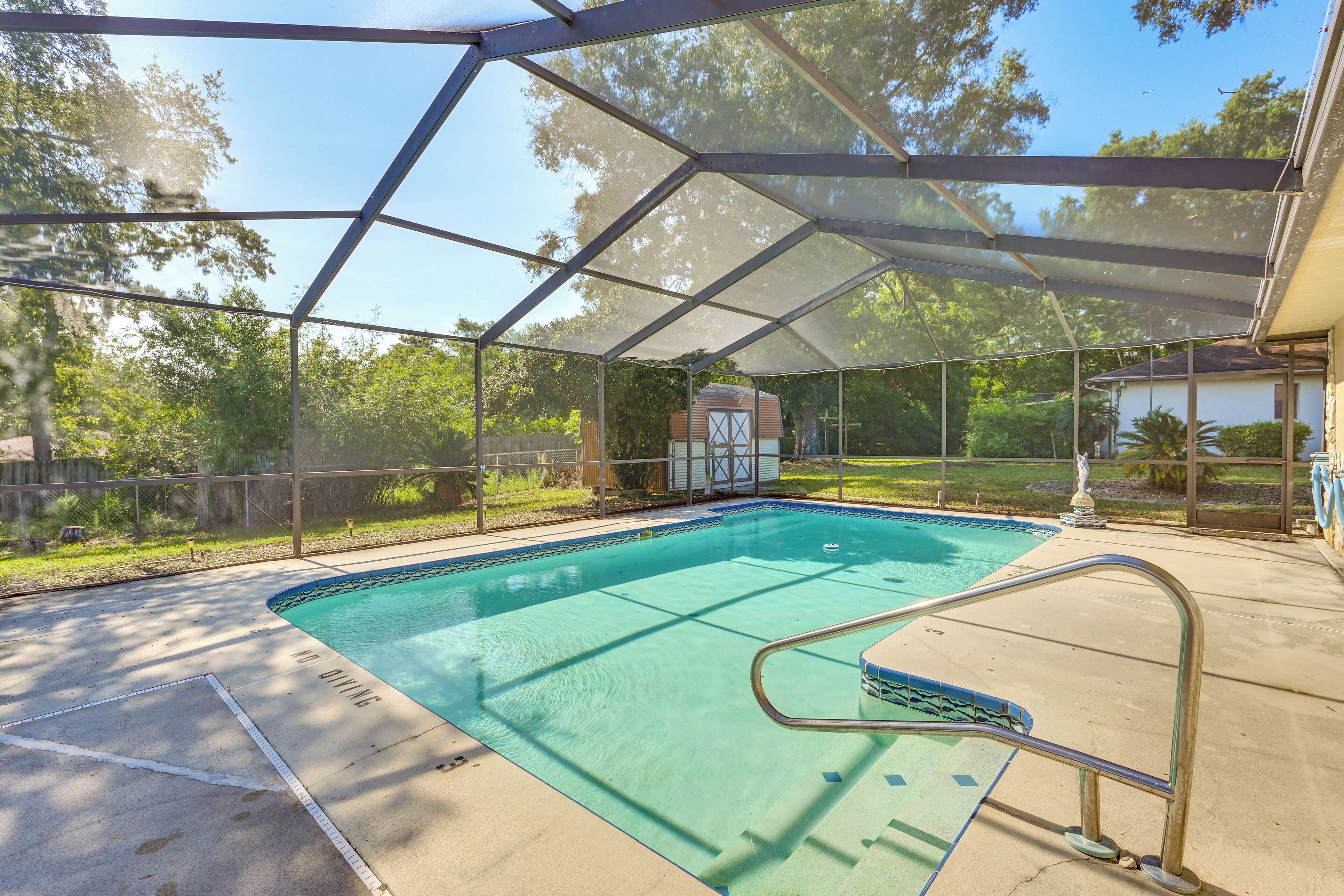 A covered outdoor swimming pool with a safety railing, surrounded by a fence and trees.