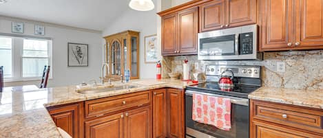 A kitchen with granite countertops, wooden cabinets, stainless steel appliances, and a large window.