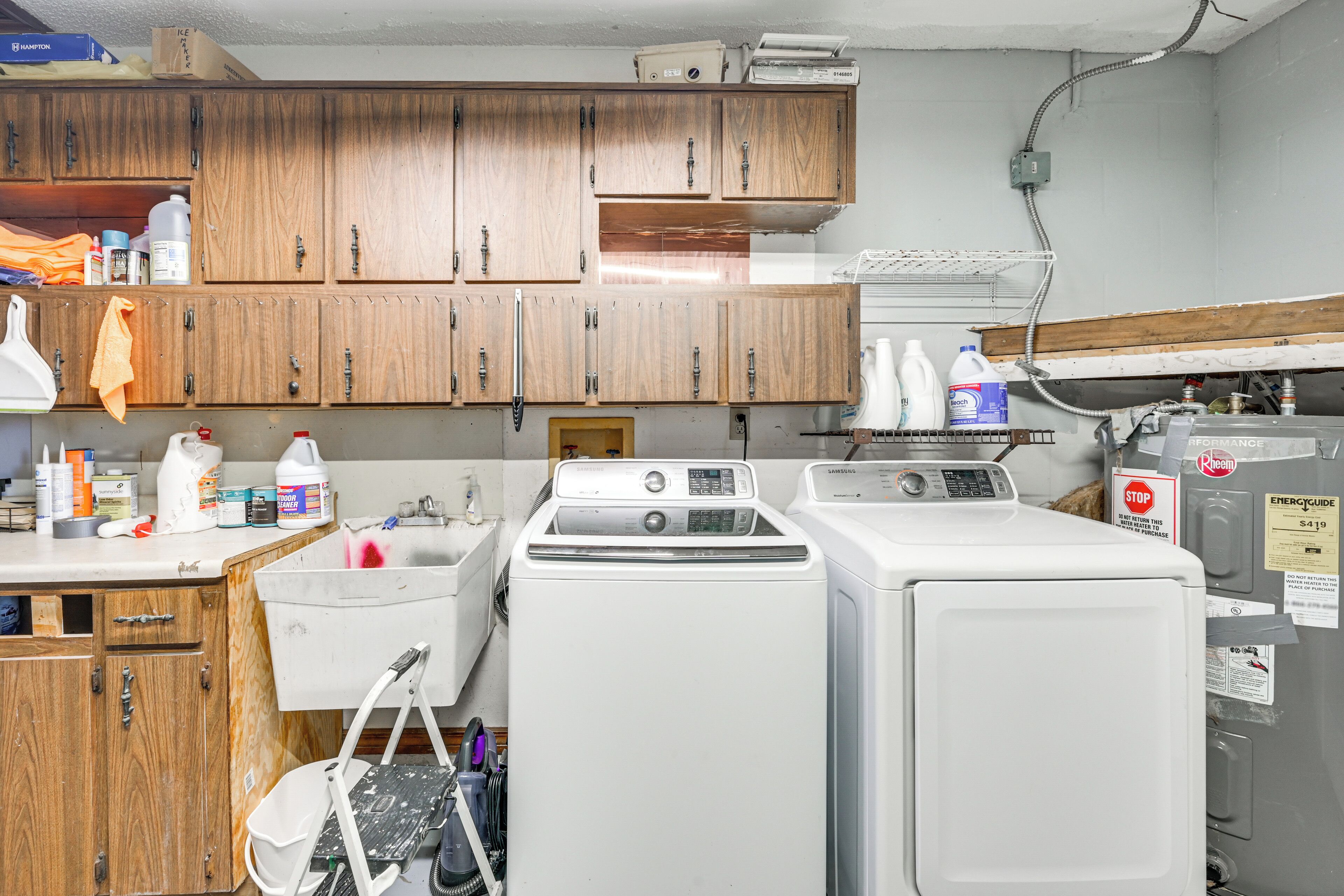A laundry room with wooden cabinets, a washing machine, a dryer, and various cleaning supplies.