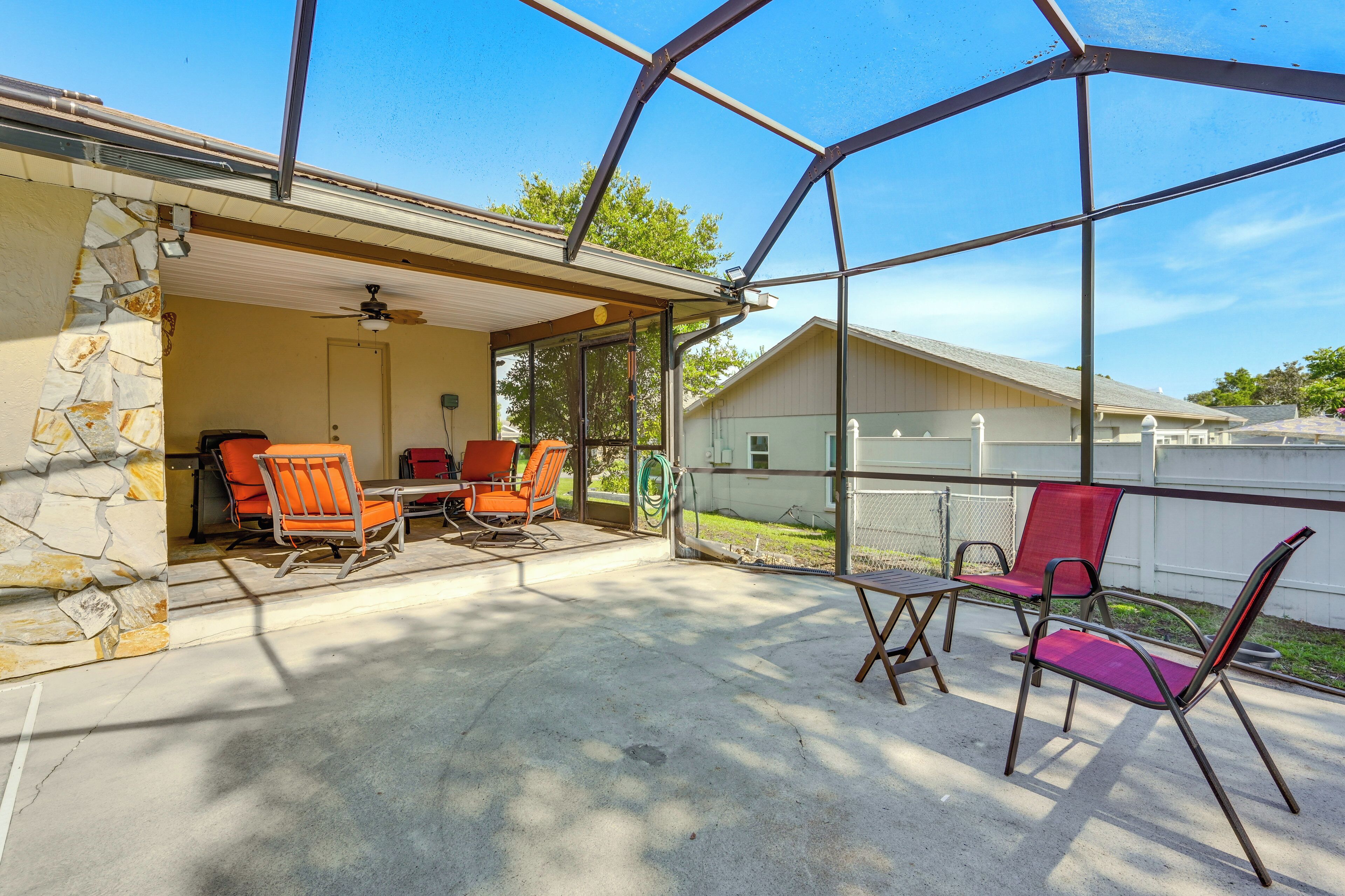 A covered patio area with stone walls, a ceiling fan, and several chairs.