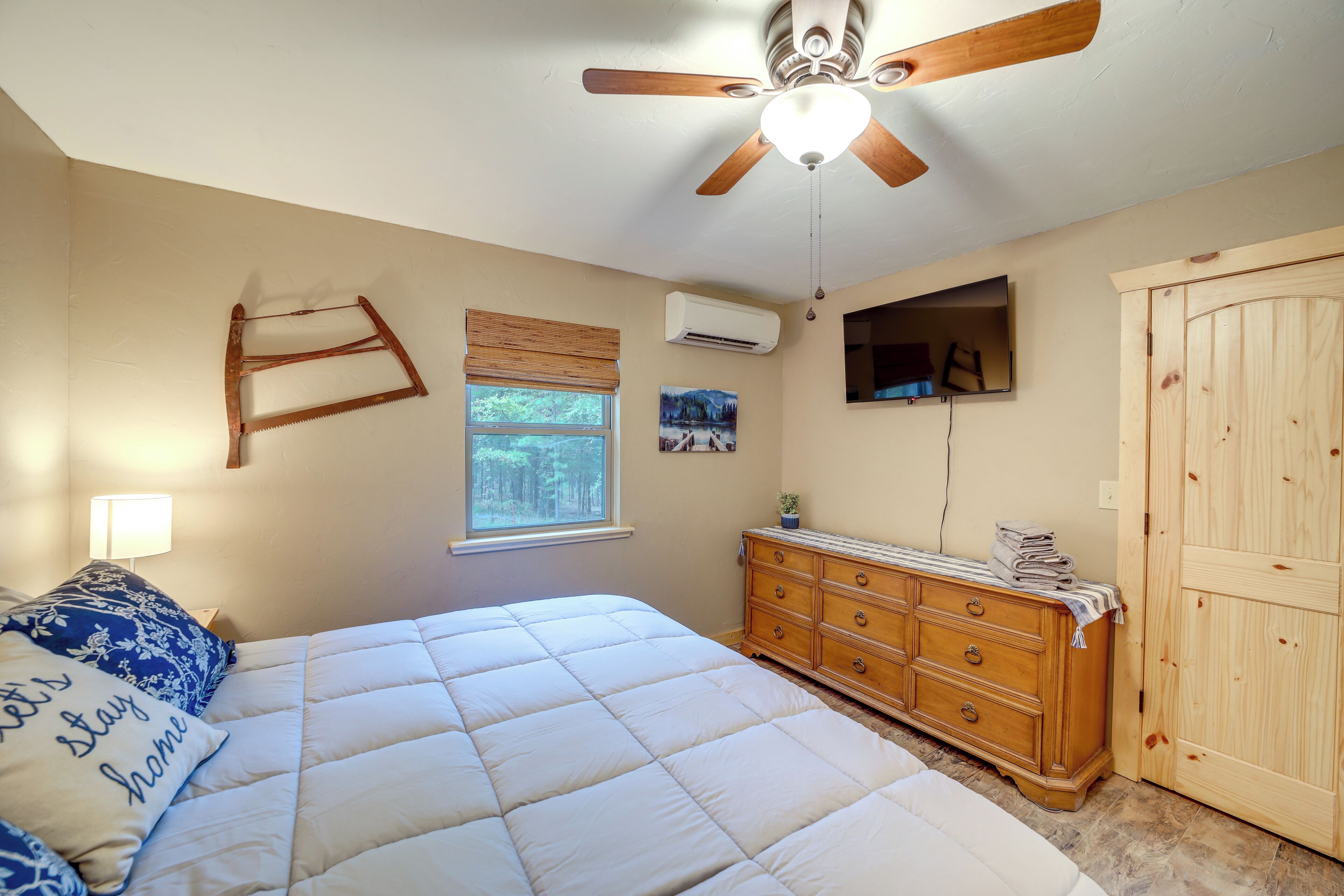 Una camera da letto con un letto, una cassettiera in legno, una ventola a soffitto, una finestra con persiane e un televisore fissato al muro.